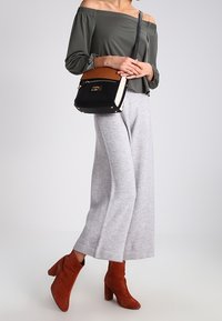 Olijfgroen off-shoulder top, grijze wijde broek, rode suède enkellaarsjes en een zwart en bruin schoudertasje met gouden hardware.