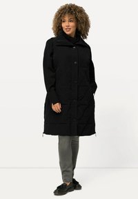 Mustat tikkivuorelliset takki napitussuljenta, vetoketjukaulus ja pitkät hihat, yhdistettynä harmaisiin housuihin ja mustiin kenkiin. Sujuva, teksturoitu kangas.