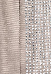 Tissu beige avec une texture tissée lisse, présentant une ligne verticale de clous en argent réfléchissants disposés de manière régulière sur un côté.