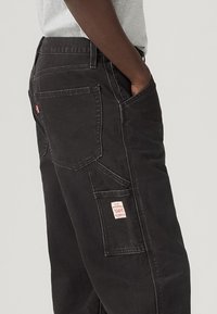 Μαύροι cargo παντελόνια με πολλαπλές τσέπες, ορατή ραφή και κόκκινη ετικέτα. Διαθέτουν άνετη εφαρμογή και ελαφριά υφή στο ύφασμα.