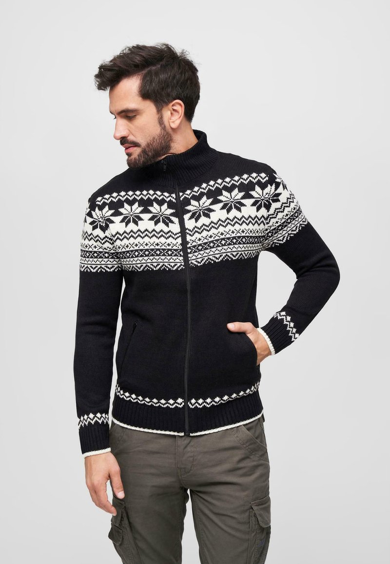 Suéter negro de punto con cierre que presenta un patrón de copos de nieve en blanco contrastante y acentos texturizados en el cuello y los puños.