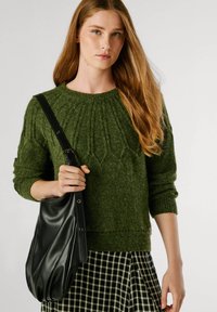 Zaļš adīts džemperis ar ribotu apkakli, apvienots ar melnu ādas plecu somu. Modelim mugurā ir raibais svārki.