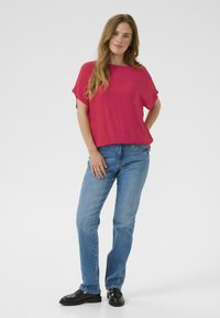 Haut fuchsia à manches courtes avec une coupe décontractée, associé à un jean droit bleu clair et des mocassins noirs, présenté sur un fond neutre.