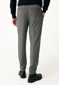 Šedé vzorované kalhoty slim fit, se dvěma zadními kapsami, s manžetami a v kombinaci s černými kotníkovými botami.