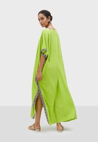 Limegrön kaftan med korta ärmar, sidofickor och mönstrad kant längs halsringning och ärmar; tillverkad av lätt tyg för komfort.