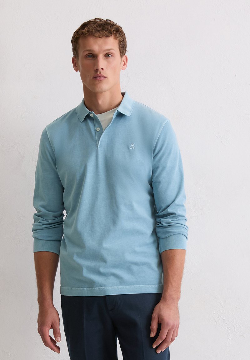 Lichtblauw poloshirt met lange mouwen, gemaakt van zachte stof, met een knoopsluiting met drie knopen en een discreet logo op de linkerborst.