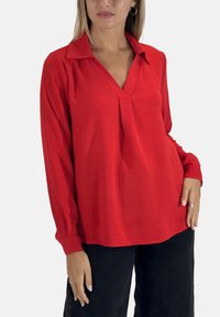 Blouse rouge à manches longues avec col et détail plissé à l'avant ; fabriquée dans un tissu texturé, avec une coupe décontractée et une couleur unie.