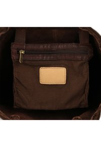 Brown leather and fabric bag interior with a zipped pocket and a small blank leather label patch, featuring a soft texture and sturdy design.