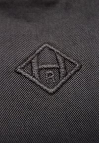 Black fabric with fine diagonal texture features an embroidered diamond logo in a slightly darker shade of black.