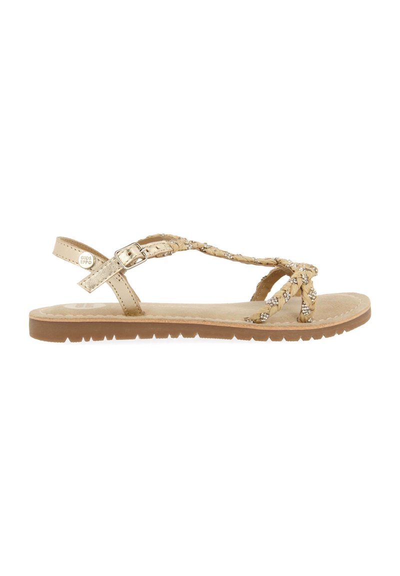 Sandalias trenzadas en color beige con acentos metálicos decorativos, una correa con hebilla ajustable y una suela plana texturizada.