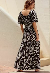 Maks haljina u crno-bijelom zebra uzorku, sa kratkim rukavima, volanima na rubu i strukom koji ističe figuru. Glatka, teksturirana tkanina.