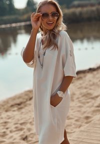 Biała, oversize'owa sukienka z krótkimi rękawami, z bocznymi kieszeniami. Noszona z srebrnym naszyjnikiem, beżowymi okularami przeciwsłonecznymi i białym zegarkiem.