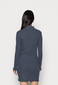 Långärmad, ribbad klänning i mörkgrått med en scallop-design vid halsringning och fåll. Tyget verkar mjukt och texturerat.