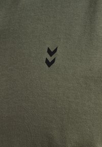 Deux chevrons noirs pointant vers le bas au centre d'un tissu vert olive, montrant la texture d'un textile tricoté.