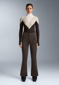 Pletený top v béžovej, bielej a tmavohnedej farbe s rebrovanou textúrou. Vysoký golier a priliehavé nohavice s rozšírenými spodnými časťami v tmavohnedej farbe.