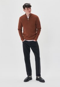 Rjav zip-up pulover z dolgimi rokavi, v kombinaciji s črnimi hlačami in črnimi loaferji. Čista zasnova, izdelan iz mehkega materiala, minimalni dodatki.