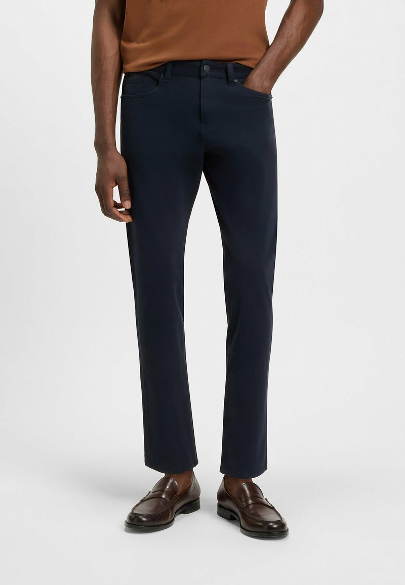 Navyblauwe broek van katoen, met een slim fit, vijf-pocket ontwerp en subtiele stikseldetails; gecombineerd met bruine loafers.