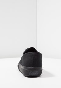 Black canvas sneaker with a textured surface, rubber sole, and logo detail on the heel. Low-top design, featuring a round toe and minimal accents.