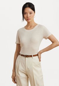 Light beige short-sleeve t-shirt made of soft fabric, featuring a round neckline and rolled cuffs, paired with high-waisted cream trousers and a brown belt.