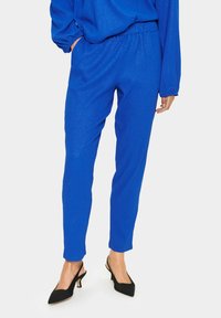Modré strukturované kalhoty s elastickým pasem, zužujícími nohavicemi a bočními kapsami, doplněné o černé lodičky na podpatku se zapínáním na patě.