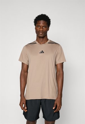 Lysbrun kortærmet sports T-shirt med sorte accenter, lavet af glat stof. Har en rund halsudskæring og et logo på brystet. Sammen med sorte shorts.