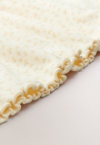 Tessuto a coste morbido con piccola stampa floreale pastello, primo piano del bordo smerlato color crema.