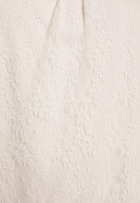 Tissu en dentelle couleur crème avec des motifs floraux complexes et une texture délicate.