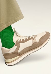 Weiße und taupefarbene Sneaker aus Wildleder und Leder, mit einer runden Zehenpartie und einer cremefarbenen Sohle, kombiniert mit einer grünen ribbed Socke.