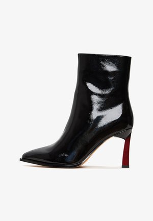 Crne patent kože gležnjače s oštrim vrhom i sjajnom završnom obradom. Potpetica je vitka i ima crveni akcent.