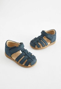 Dunkelblaue Ledersandalen mit offenen Zehen, ausgestattet mit breiten Riemen und einem Klettverschluss. Helle braune Einlegesohlen und gummierte Sohlen sind sichtbar.