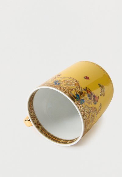 Κίτρινο κεραμικό φλιτζάνι που έχει αναποδογυρίσει, με περίτεχνα σχέδια πεταλούδας, πασχαλίτσας και λουλουδιών, και χρυσή λαβή, σε λευκό φόντο.