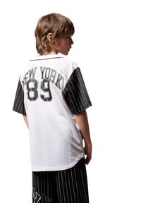 Maillot à manches courtes blanc avec des manches rayées noires, avec "NEW YORK" et "89" imprimés en noir à l'arrière.