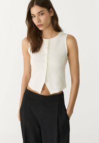 Witte, mouwloze cropped top met een ronde halslijn en een knoopsluiting aan de voorkant. Zachte stof met een lichte glans en een getailleerde pasvorm.