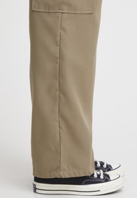 Beige bomullbyxor med rak skärning, med sidofickor och en mjuk textur, tillsammans med svart och vit kanvas sneakers.
