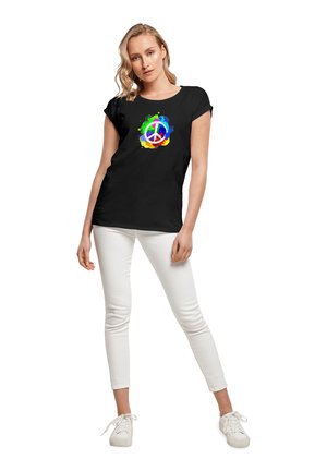 Sort T-shirt med korte ærmer, prydet med et flerfarvet fredssymbol grafisk design omgivet af farvesplash. Sammen med hvide bukser.