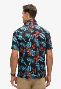 Camisa de manga corta negra con un patrón de hojas y flores tropicales en azul y rojo. Tejido suave con cuello estándar y dobladillo recto.