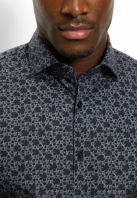 Hemden mit Knöpfen, die ein marineblaues Muster mit hellblauen geometrischen Formen aufweisen. Der Stoff hat eine glatte Textur, mit klassischem Kragen und einzelnen Knöpfen.