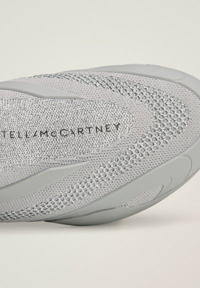 Gros plan sur une basket grise en tricot avec des motifs texturés et le texte "STELLA McCARTNEY" imprimé sur la surface supérieure.
