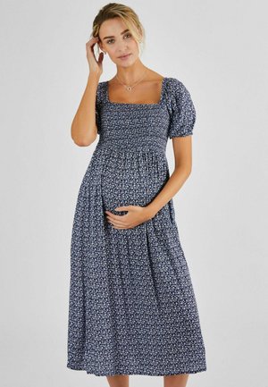 Robe florale bleu marine avec des manches courtes bouffantes, un décolleté carré et un buste smocké, descendant jusqu'à une jupe au genou. Tissu doux et léger.
