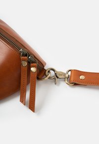 Braune Ledertasche mit Reißverschluss, ausgestattet mit Messingbeschlägen, doppelten Reißverschluss-Ziehentlastungen und einem abnehmbaren Riemen mit Druckknopf-Haken.