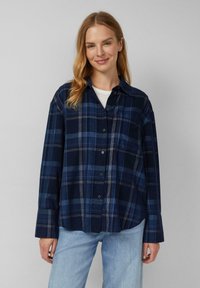 Marineblauwe geblokte shirt met knopen aan de voorkant, lange mouwen en een ontspannen pasvorm. Kenmerkt zich door witte en lichtblauwe accenten in het patroon.