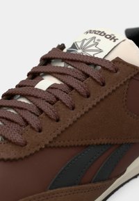 Kohvade sametist ja kangast tenniset jalatsid, tumeate paeltega, mustade logo triipudega ja valge keelekese ning Reeboki kaubamärgi ja embleemiga.