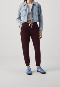 Abgeschnittene Jeansjacke, hellblau; weißes Crop-Top; bordeauxfarbene Jogginghose mit Kordelzug; blaue Sneakers mit grauen Akzenten.