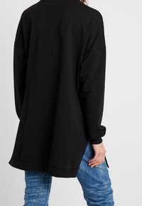 Felpa nera oversize con maniche lunghe, polsini a coste e orlo rotondo. Abbinata a jeans azzurri chiari con vestibilità comoda.