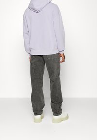 Sweat à capuche lilas avec une coupe décontractée et une capuche, associé à un jean gris taille haute, ample, et des chaussures blanches à semelle épaisse.