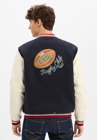 Marineblau und cremefarbene Varsity-Jacke mit geripptem Kragen, auf der Rückseite mit einem bestickten Rugbyball und "FHL Rugby Club".