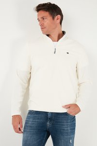 Hele koor pullover, millel on poolelukk, pikkade varrukatega ja väikese logodetailiga rinnal, koos siniste teksadega. Pehme tekstuur.