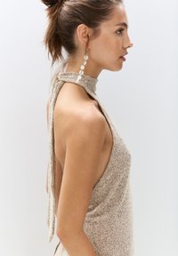 Beige, sleeveless dress with a high neckline and open sides, featuring a textured knit fabric and a tie detail at the back.