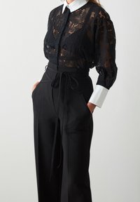 Czarna koronkowa bluzka z długim rękawem i białym kołnierzykiem, połączona z czarnymi spodniami o wysokim stanie z bocznymi kieszeniami i paskiem do zawiązywania.