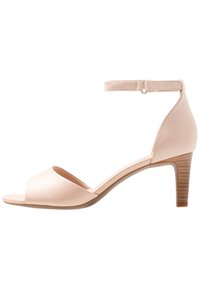 Sandale à talons hauts en cuir nude avec orteil ouvert, sangle de cheville et talon en bois texturé. Surface lisse avec un design minimaliste.